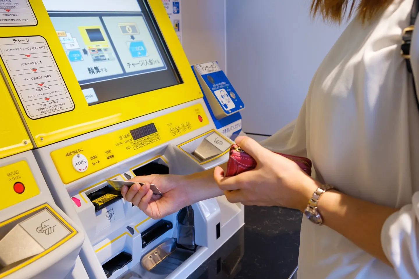 امرأة تستخدم ماكينة Fare Adjustment الصفراء في محطة يابانية لدفع فرق الرصيد وشحن البطاقة